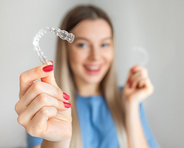 woman holding Invisalign with her face blurred in the background 