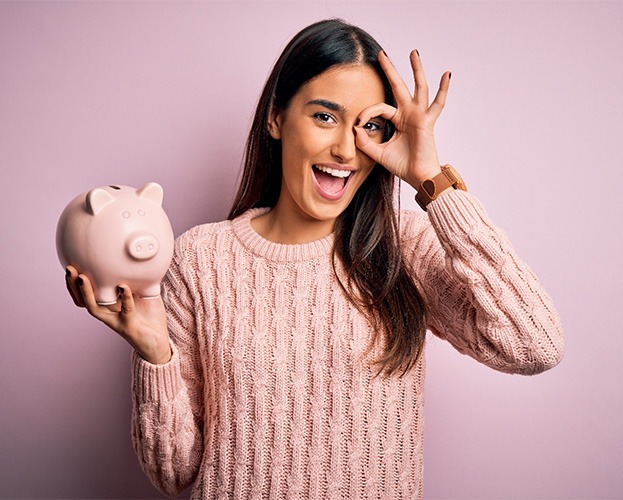 Woman smiling and holding a piggy bank and holding an okay sign on her face