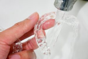 hands rinsing off Invisalign aligners under water
