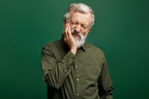 older man holding his face in discomfort with a green background